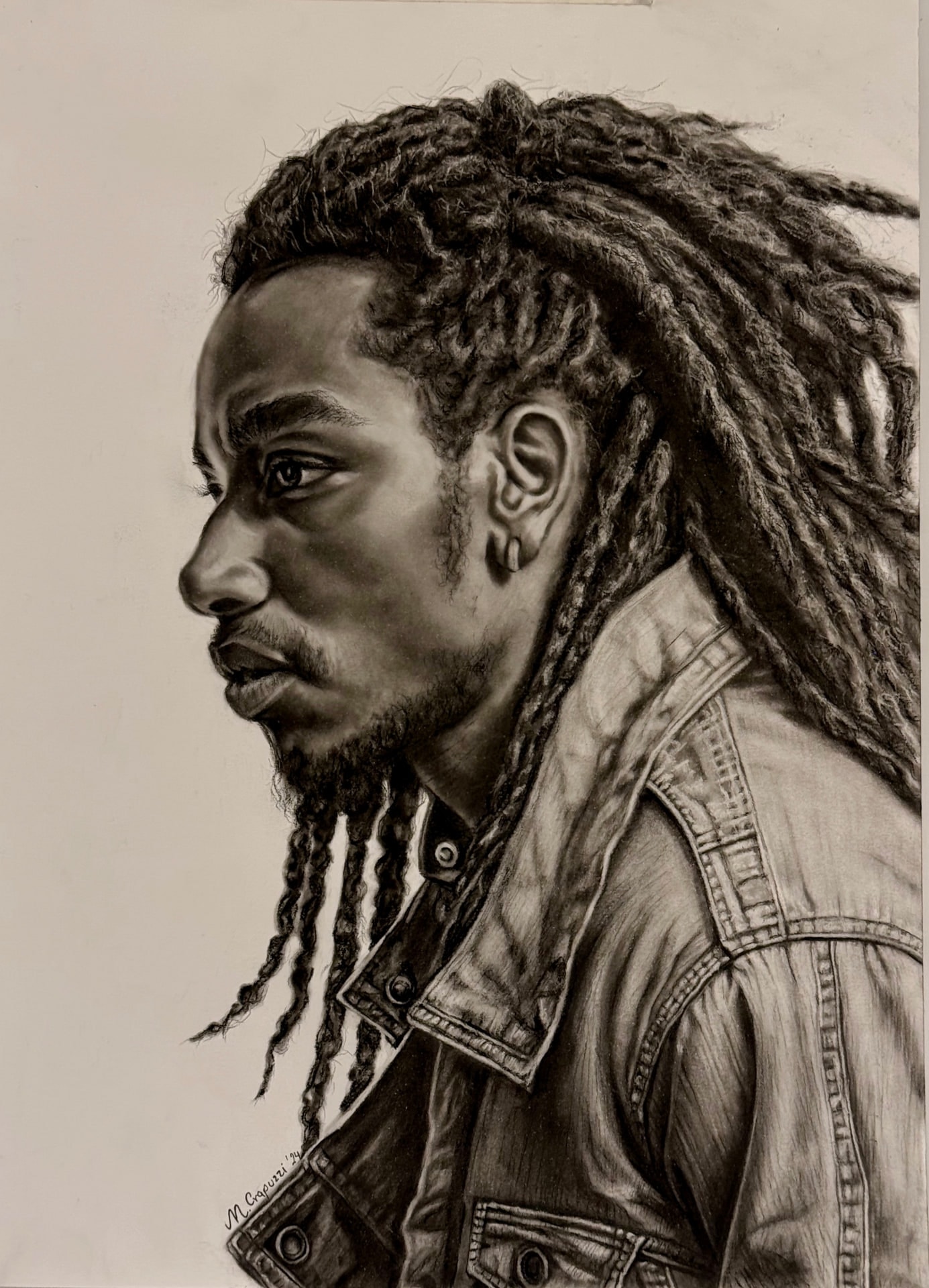 Carboncillo de un hombre de perfil con rastas largas y chaqueta de jean, la mirada dirigida fuera del encuadre.